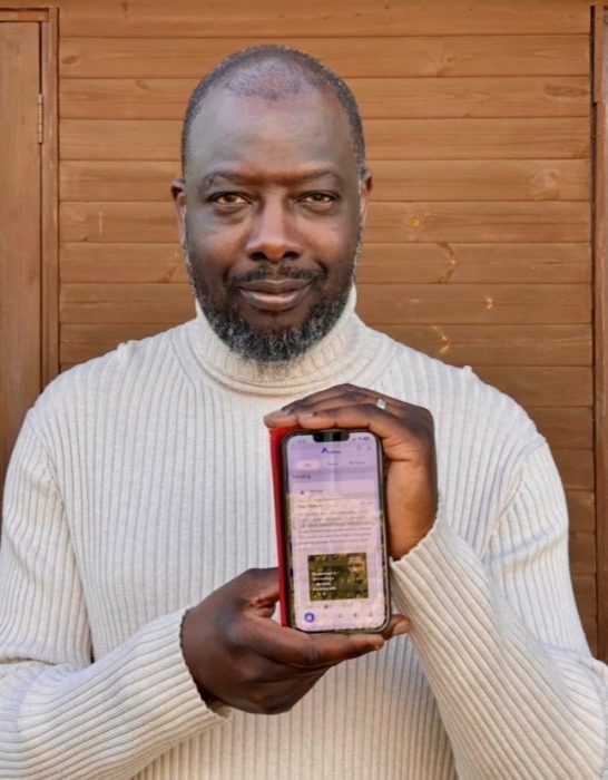 ReAktu founder Remmy stands with a phone displaying the home page of his social media app